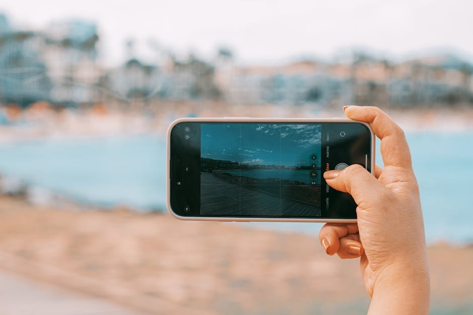 pexels-photo-28243791-28243791 Hand holding smartphone capturing a scenic beach view in Palma de Mallorca.