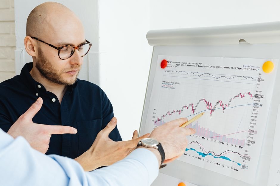 pexels-photo-7876668-7876668 Business professionals discussing financial graphs on a flipchart during a daylight meeting.